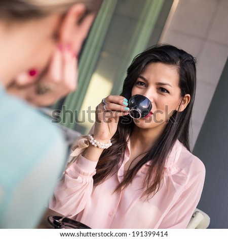 Young brunette woman drinking coffee with friend in a cafe outdoors. Shallow depth of field.