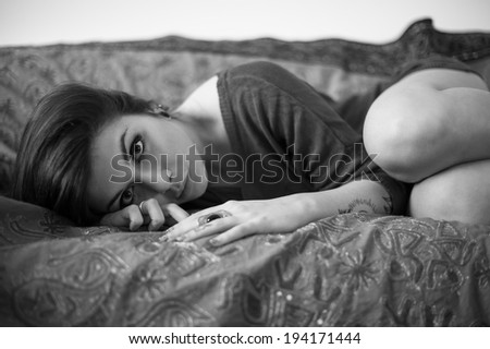 Sensual portrait of beautiful girl with tattoo lying on sofa. Black and white image.