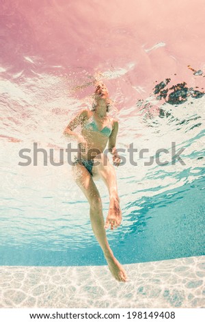 Woman wearing bikini underwater in swimming pool.