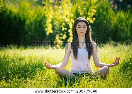 Beautiful young woman doing yoga, sitting in lotus position on green grass. Concept of healthy lifestyle and relaxation. Filtered image.