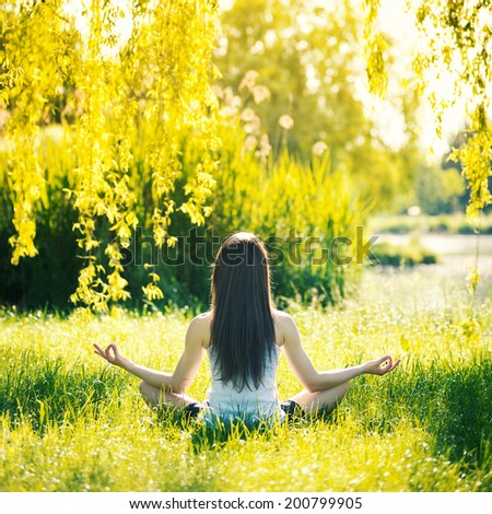 Back view of young woman doing yoga, sitting in lotus position on green grass. Concept of healthy lifestyle and relaxation. Filtered image.