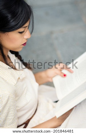 Beautiful brunette woman reading a book outdoors.