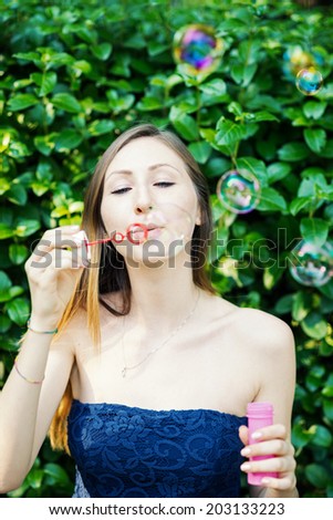 Young woman portrait with soap balloons against natural green hedge background.