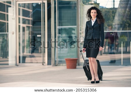 Business woman outdoors walking with trolley. Full body portrait.