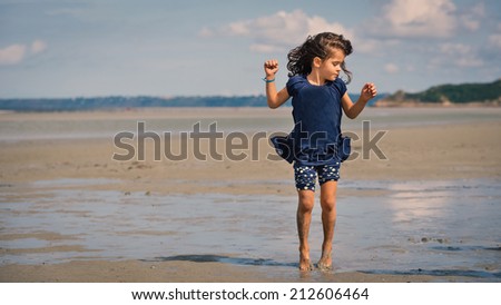Young girl having fun on the beach in front of Mont Saint Michel ancient village. Normandy, France.