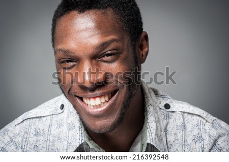 Laughing black man close up portrait against grey background.