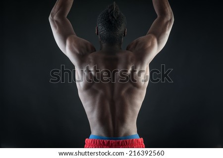 Strong young black man shirtless portrait against black background. Back view.