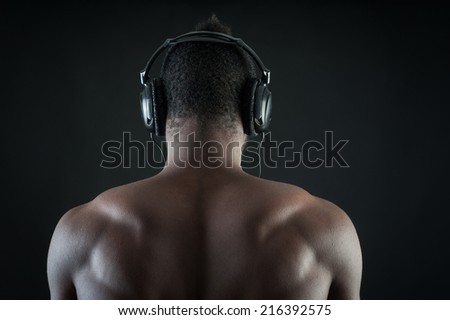 Black man with ear-phones detail against dark background. View from behind.