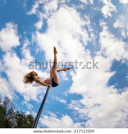 Attractive sexy woman pole dancer performing outdoors against blue cloudy sky. Filtered image.