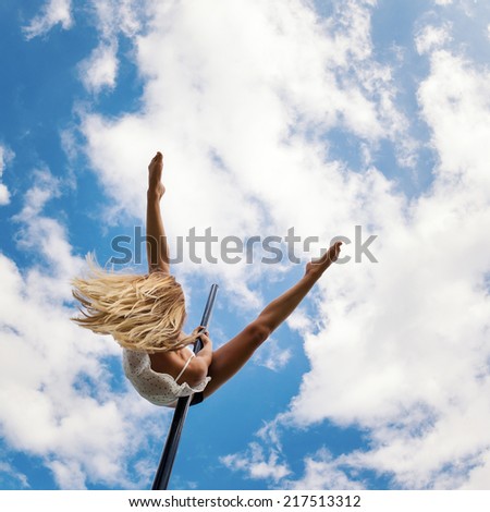 Attractive sexy woman pole dancer performing outdoors against blue cloudy sky. Filtered image.