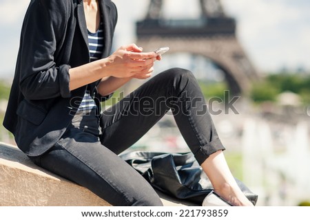 Deteail of young woman using mobile phone in front of the Eiffel Tower. Paris, France. Filtered image.