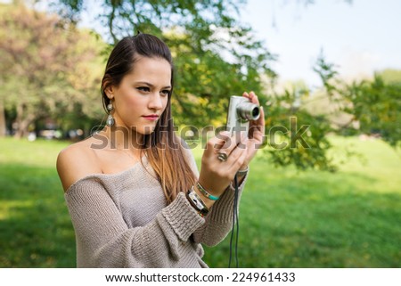Portrait of young woman with compact camera outdoors in a park.