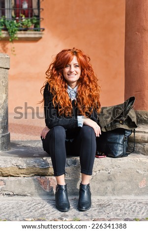 Smiling redhead woman portrait sit outdoors in the street.
