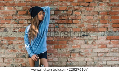 Teenager portrait with skateboard against brick wall with copy space.