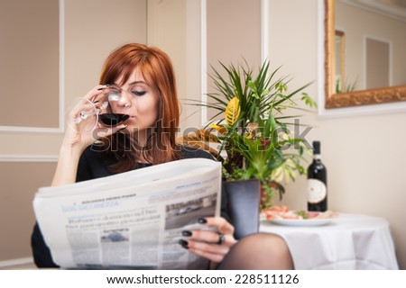 Young redhead business woman reading newspaper with a glass of wine in a hotel.