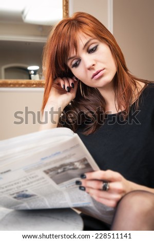 Young redhead business woman reading newspaper in a hotel.