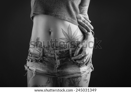 Close up of beautiful woman hands with tattoo wearing jeans short paint against black background. Black and white image.