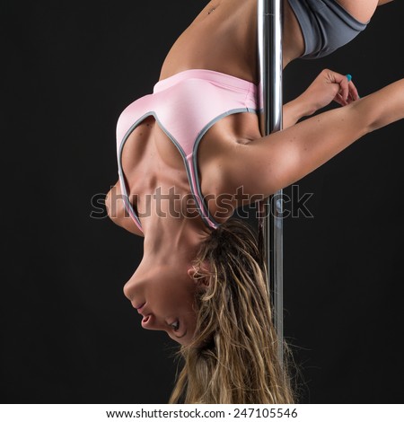 Beautiful woman performing pole dance upside down. Studio shot on black background.