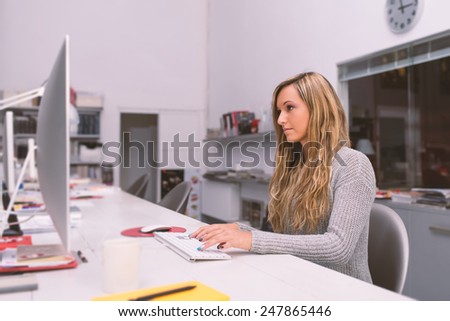 Young woman portrait working with computer in modern office. Filtered image.