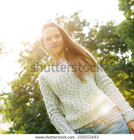 Beautiful young woman close up portrait with natural green background relaxing in a park. Filtered image with back light effect.
