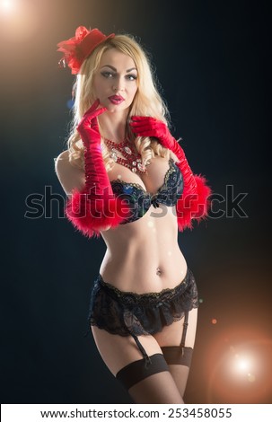 Portrait of a busty woman in vintage black bra and red gloves. Studio shot with back light effect on black background.