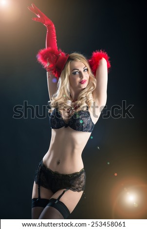 Portrait of a busty woman in vintage black bra and red gloves. Studio shot with back light effect on black background.