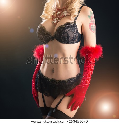 Close-up shot of a busty woman in vintage black bra and red gloves. Studio shot with back light effect on black background.