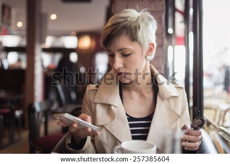 Young woman sending message with cellular phone in a cafe in Paris, France. Shallow depth of field.