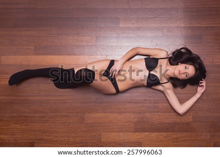Sensual woman portrait laying on parquet floor with black underwear. Full body portrait.