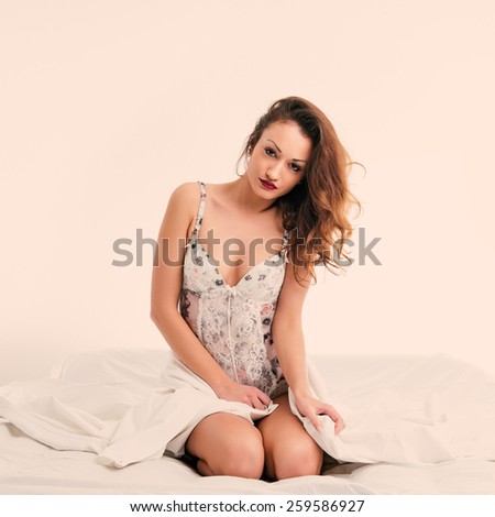 Portrait of a sensual young woman sit on bed wearing flowers wreath. Filtered studio image.