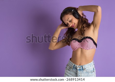 Beautiful young curly woman with headphones against purple background.