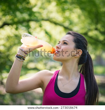 Young woman drinking energy drink outdoors in a park.