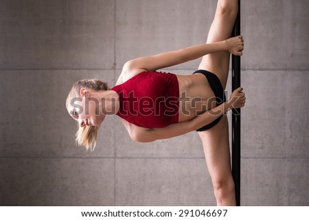 Beautiful woman performing pole dance. Shot with industrial concrete background.