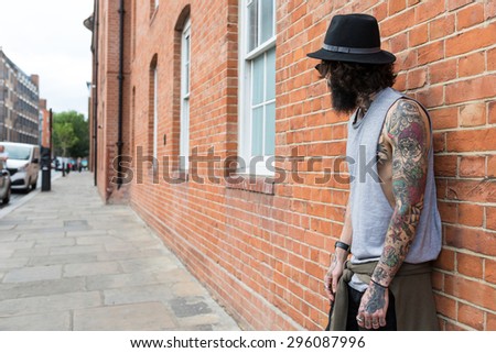 Young tattooed man portrait against brick wall in Shoreditch borough. London, UK. Hipster style