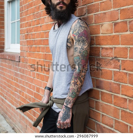 Young tattooed man portrait against brick wall in Shoreditch borough. London, UK. Hipster style
