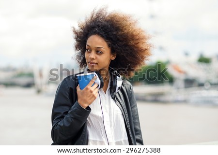 Young woman portrait outdoors on Westminster Bridge in London with coffee cup and headphones.