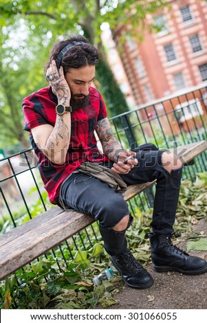 Young tattooed man portrait with head phones in a park in Shoreditch borough. London, UK. Hipster style.
