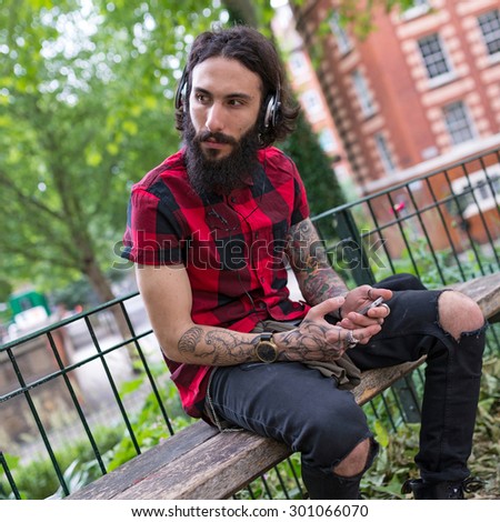 Young tattooed man portrait with head phones in a park in Shoreditch borough. London, UK. Hipster style.