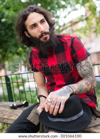 Young tattooed man portrait in a park in Shoreditch borough. London, UK. Hipster style.