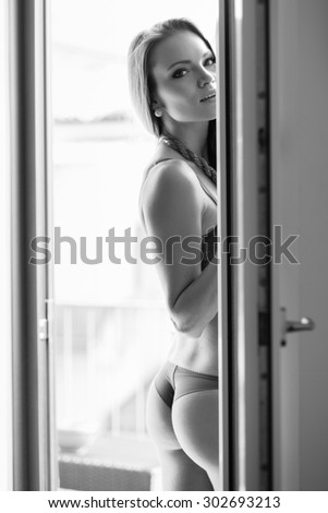 Sensual young woman portrait wearing lingerie at the window in hotel room. Black and white image.