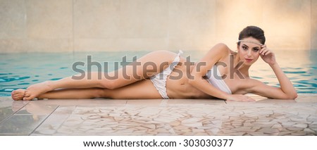 Sensual full body portrait of beautiful brunette woman wearing white bikini in swimming pool. Filtered image.