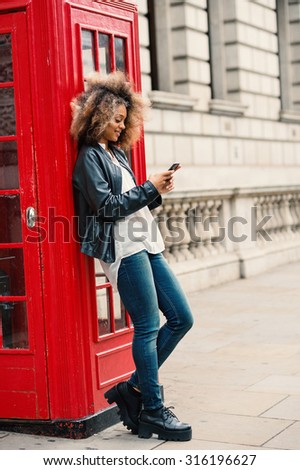 Young woman using smart phone close to red telephone box in London. Full body portrait.