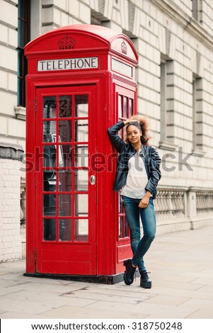 Young woman close to red telephone box in London. Full body portrait.