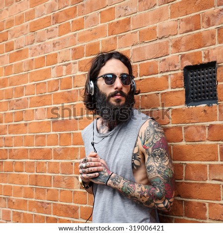 Young tattooed man portrait listening to music against brick wall in Shoreditch borough. London, UK. Hipster style.