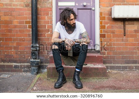 Intense portrait of young tattooed man sit on the street in Shoreditch borough. London, UK. Hipster style