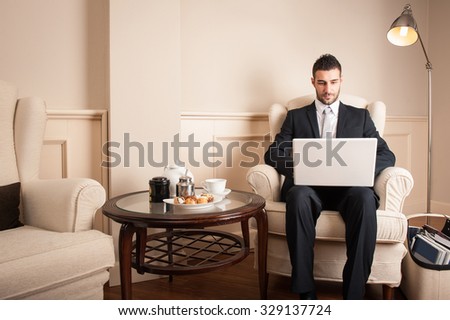Young businessman working with portable computer sit on armchair inside luxury hotel.