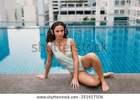 Sensual woman portrait wearing swimsuit and listening to music with headphones in swimming pool in Bangkok, Thailand. Filtered image.