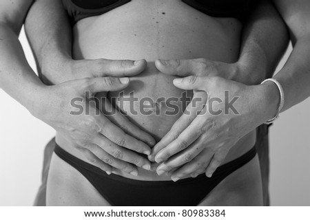 Pregnant woman and husband making heart shape with hands. Black and white photo.