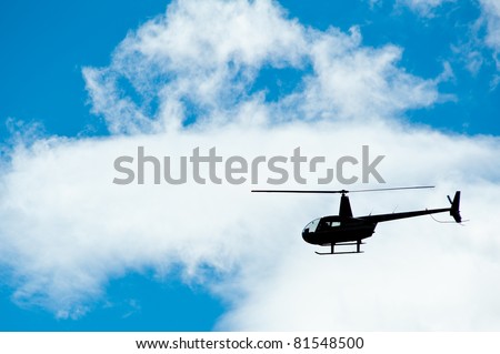 Helicopter silhouette with blue sky and clouds.