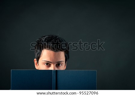 Young man behind a book against dark background.